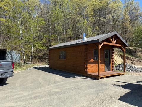 Stained log cabin with covered porch by the woods