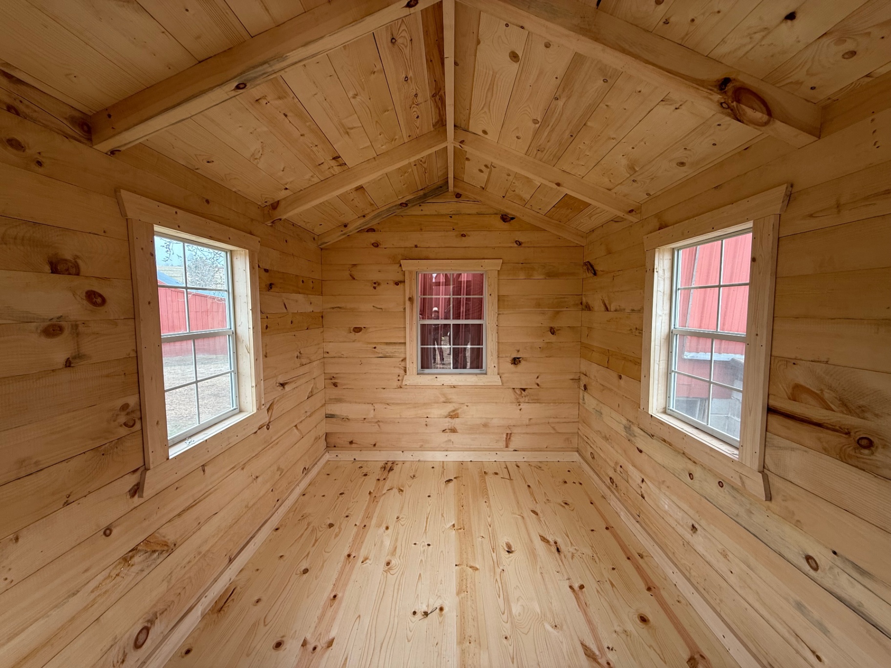 Bright cabin interior with vaulted pine ceiling and three windows